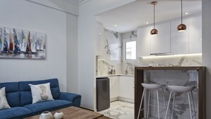 A modern living room with a blue sofa, a wooden coffee table, and a kitchen area with marble countertops and two bar stools. - Cozy and Bright Apartment in Kolonaki (Athens)
