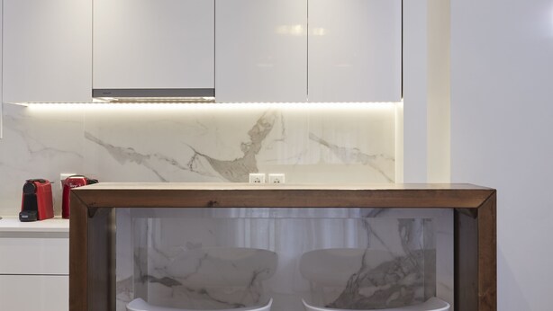 A modern kitchen with marble countertops, a wooden frame around the sink, and overhead lighting. - Cozy and Bright Apartment in Kolonaki (Athens)