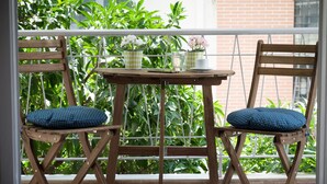 A wooden chair and table set on a balcony with a view of green plants and a brick wall. - Cozy and Bright Apartment in Kolonaki (Athens)