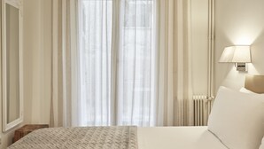 A hotel room with a bed, a bedside lamp, a radiator, and sheer curtains. - Cozy and Bright Apartment in Kolonaki (Athens)
