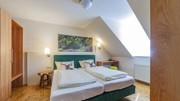 A bedroom with a green bed, two white pillows, a headboard with a deer print, a nightstand, a desk, and a window with a view of trees.