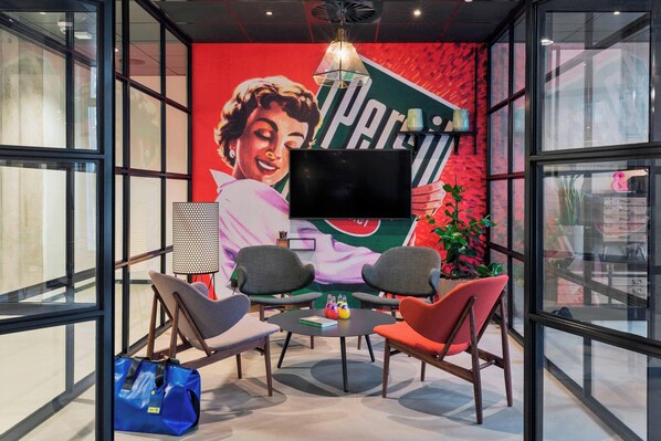 Un área de descanso moderna con una gran pantalla de televisión, asientos cómodos y un mural llamativo.