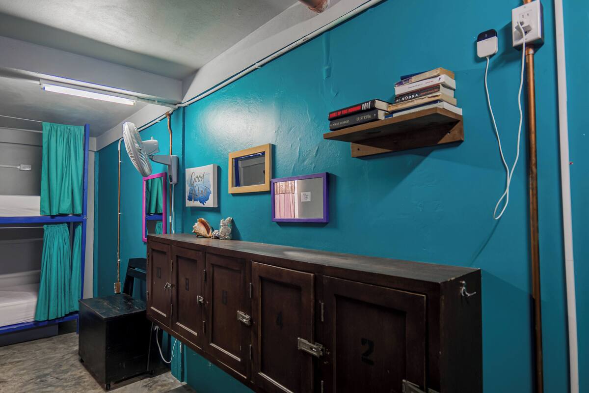 A room with bunk beds, a desk, a mirror, and a wall-mounted shelf with books.