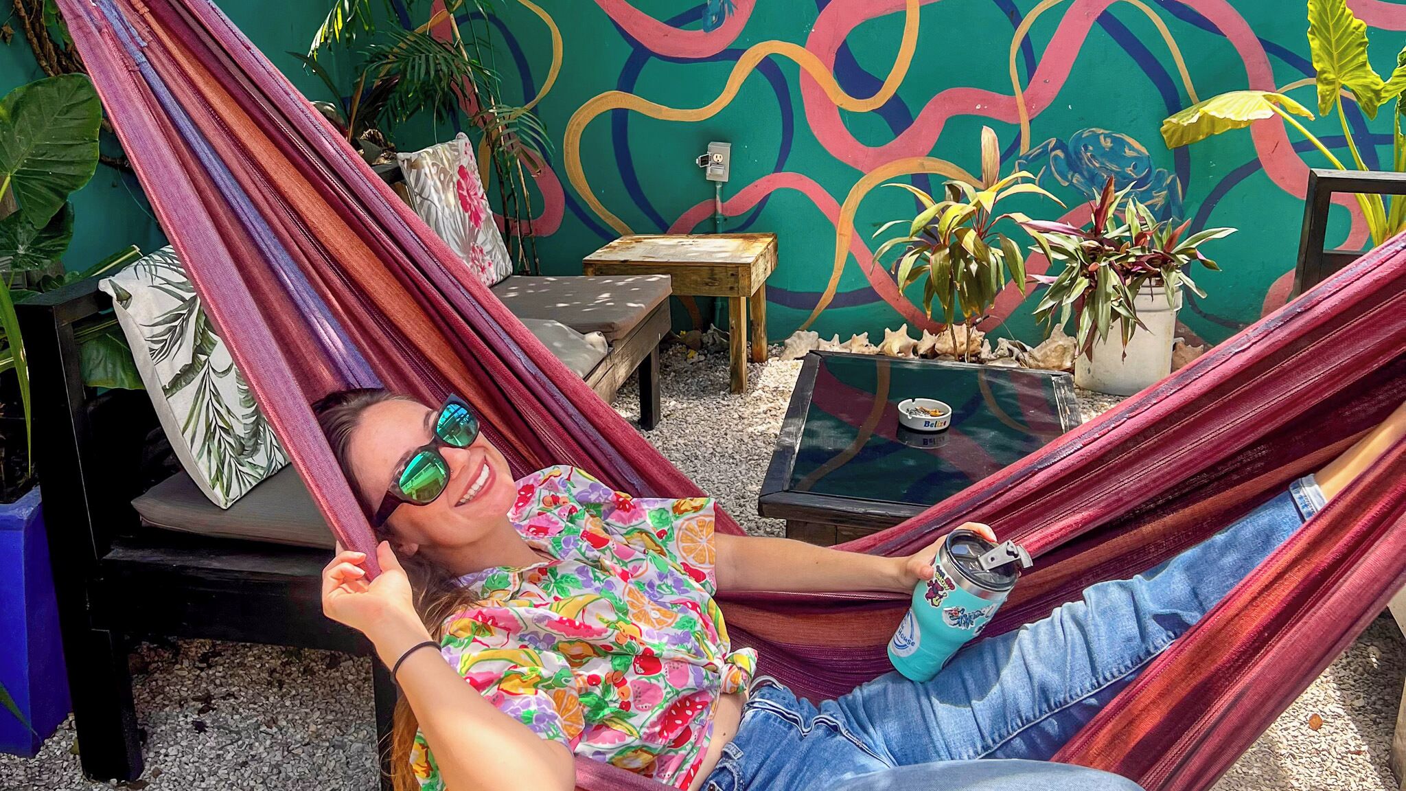 Una persona relajándose en una hamaca con un muro colorido y plantas de fondo.