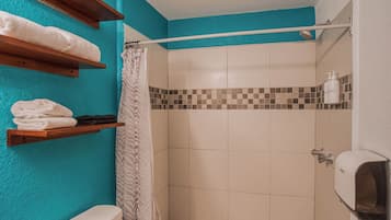 Un baño con ducha, inodoro y repisas con toallas.