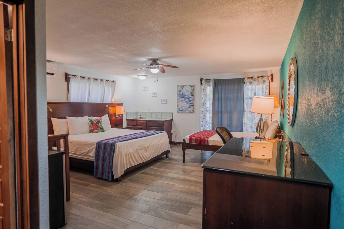 A hotel room with a bed, a desk, a chair, a ceiling fan, and a window with curtains.