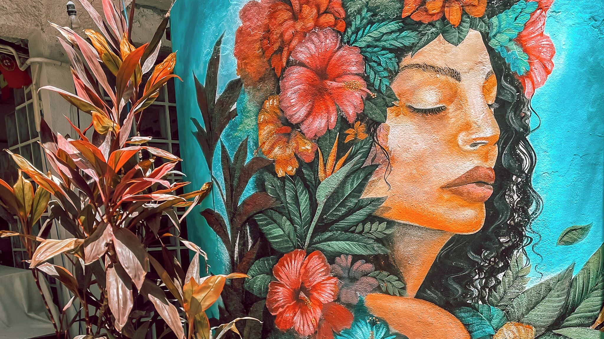 A mural with a woman's portrait surrounded by vibrant flowers and foliage.