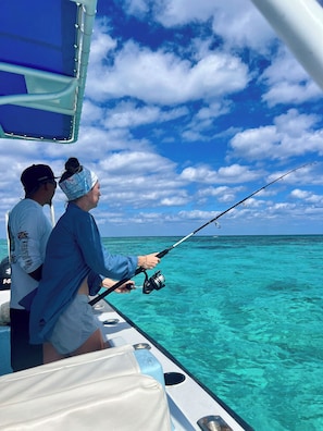 A boat with two people fishing, clear turquoise water, and a partly cloudy sky. - Drift Inn San Pedro (San Pedro)