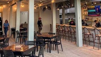 A restaurant interior with multiple tables and chairs, a bar area, and a kitchen in the background.