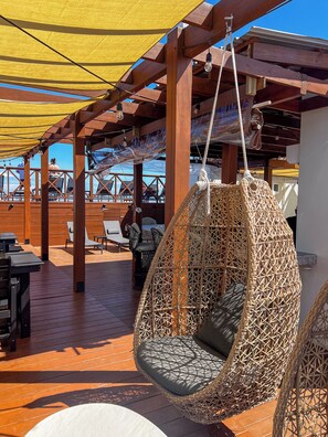 A wooden deck with outdoor seating, including a hanging chair and tables. - Drift Inn San Pedro (San Pedro)