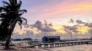 A beach with a wooden pier, a small blue building, and palm trees. - Drift Inn San Pedro (San Pedro)