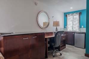 A compact office space with a wooden desk, a chair, a small refrigerator, and a mirror on the wall. - Drift Inn San Pedro (San Pedro)