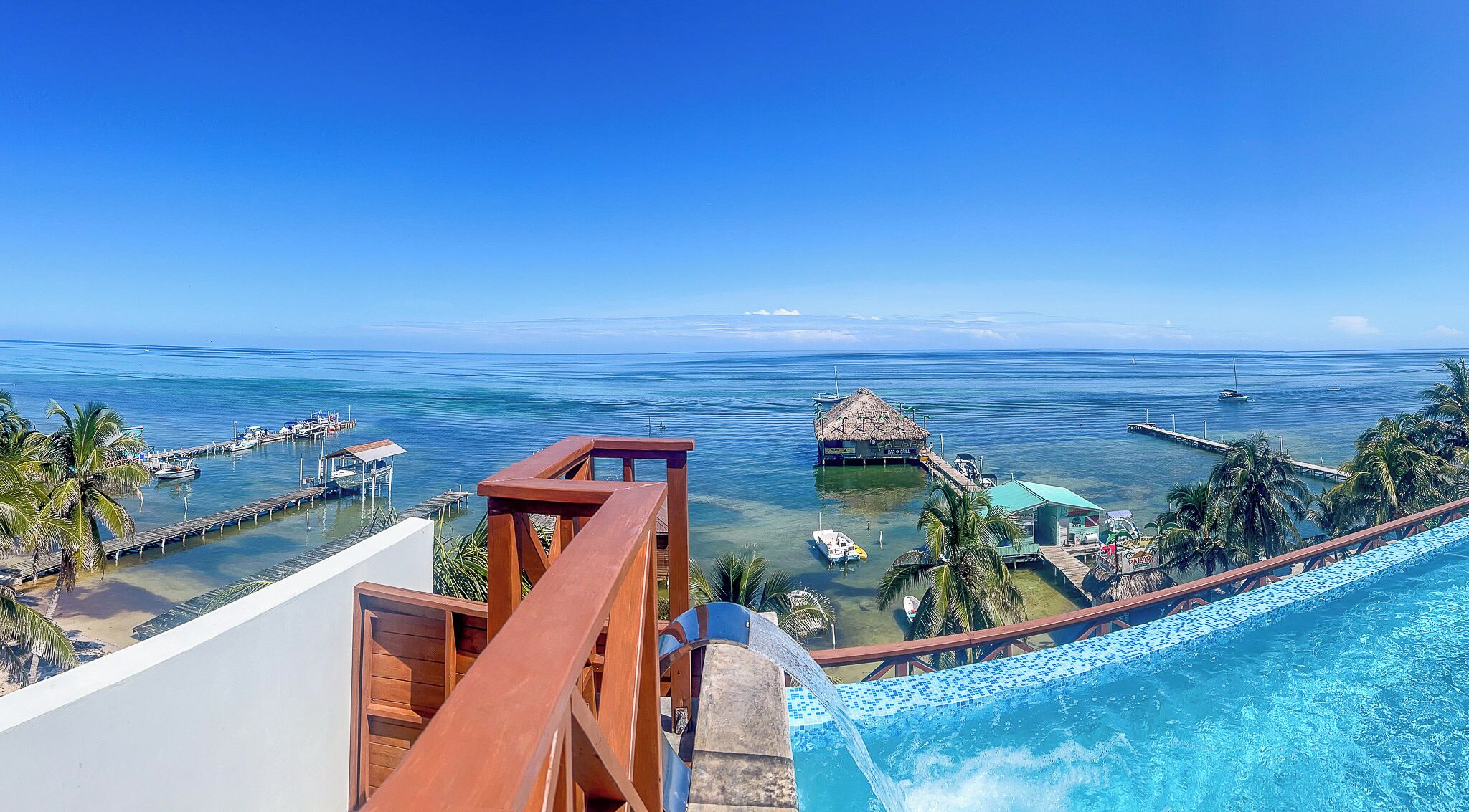 A resort with a pool, a view of the ocean, and a thatched-roof structure.