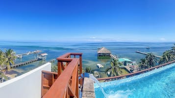 A resort with a pool, a view of the ocean, and a thatched-roof structure.