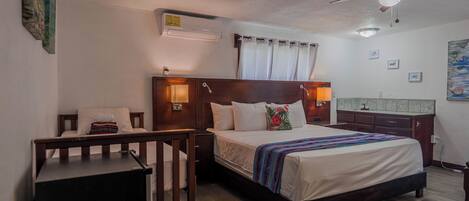A bedroom with a bed, bedside tables, a desk, a ceiling fan, and a small bathroom area.