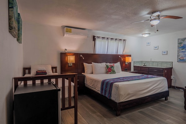 A bedroom with a bed, bedside tables, a desk, a ceiling fan, and a small bathroom area. - Drift Inn San Pedro (San Pedro)