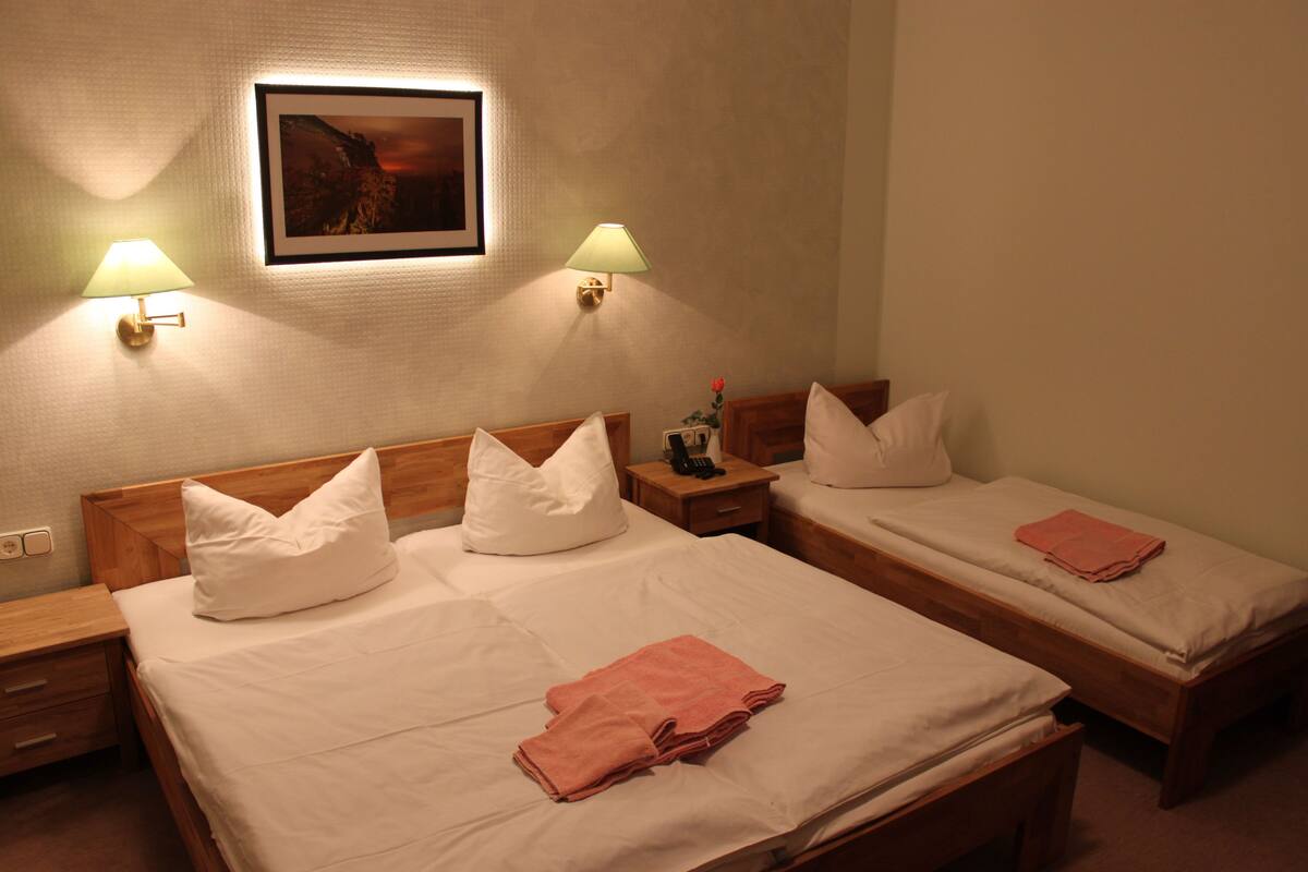 A hotel room with two single beds, a nightstand with a lamp, and a framed picture on the wall.