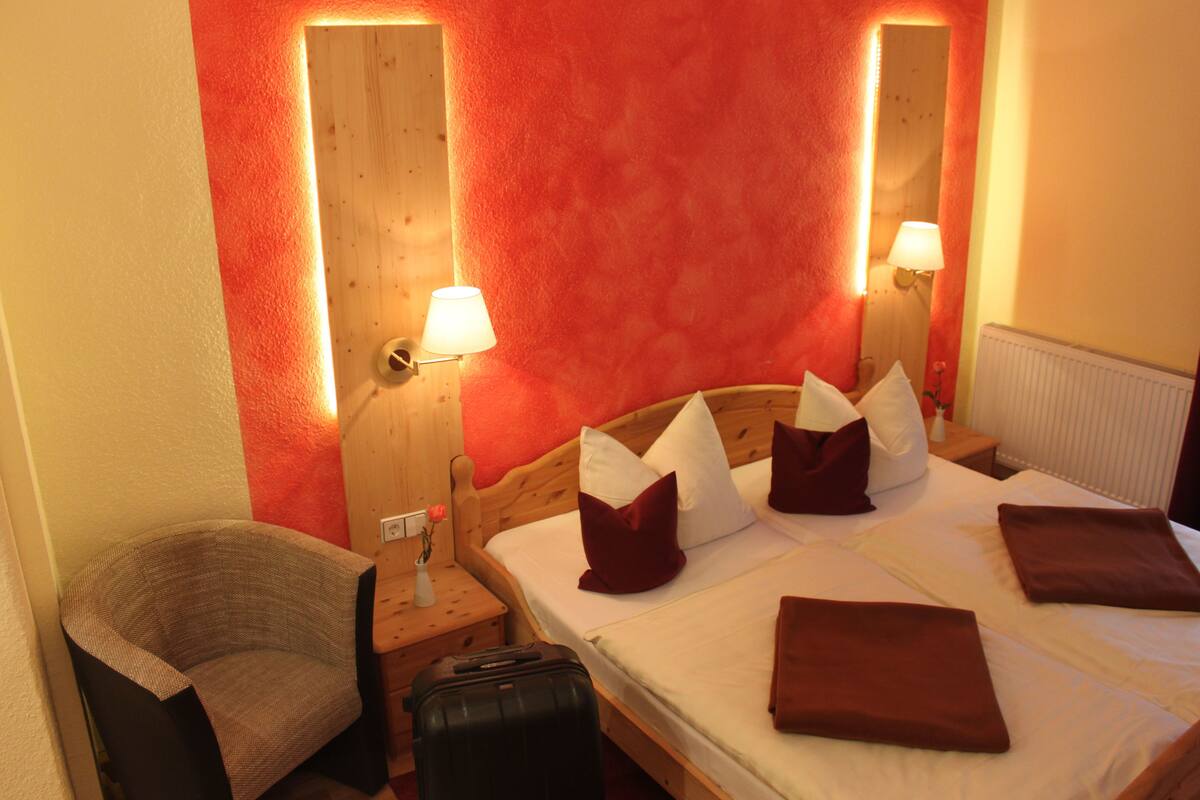 A hotel room with a wooden bed, a chair, a nightstand, and a lamp.