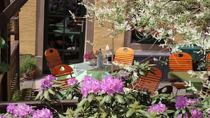 Un espace extérieur aménagé avec des chaises et des tables en bois, entouré d’arbustes en fleurs.
