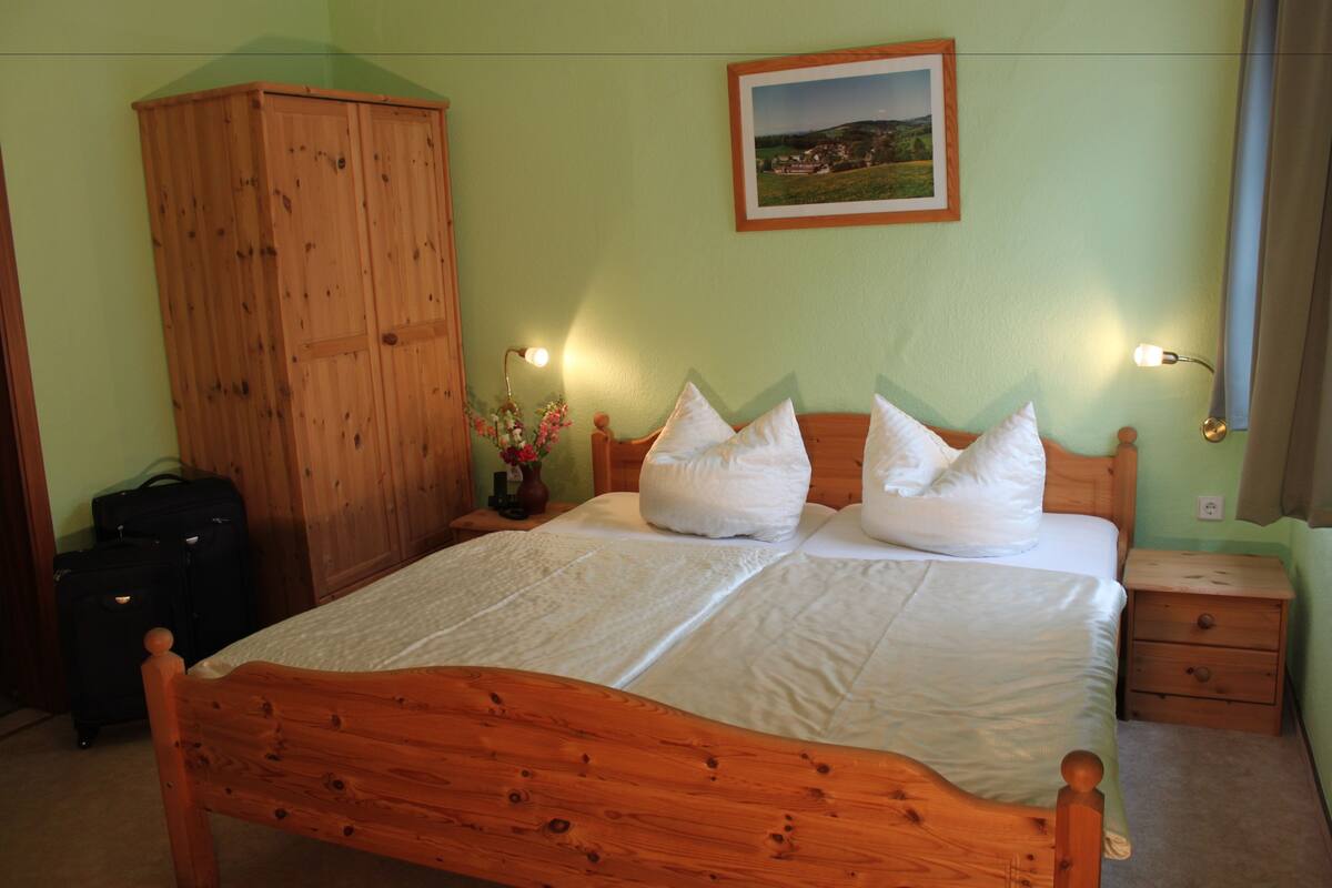 A bedroom with a wooden bed, a nightstand, a wooden wardrobe, and a picture on the wall.