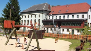 Un terrain de jeux avec des balançoires et un toboggan, un bâtiment avec un toit rouge et un ciel bleu clair.