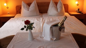 Une chambre d’hôtel avec un lit, deux tables de chevet, un vase contenant une rose rouge, deux verres à vin et une bouteille de champagne dans un seau à glace.