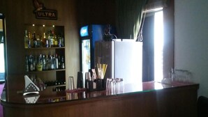Un espace bar comprenant un comptoir où sont exposées les bouteilles, un réfrigérateur et une fenêtre avec des rideaux.