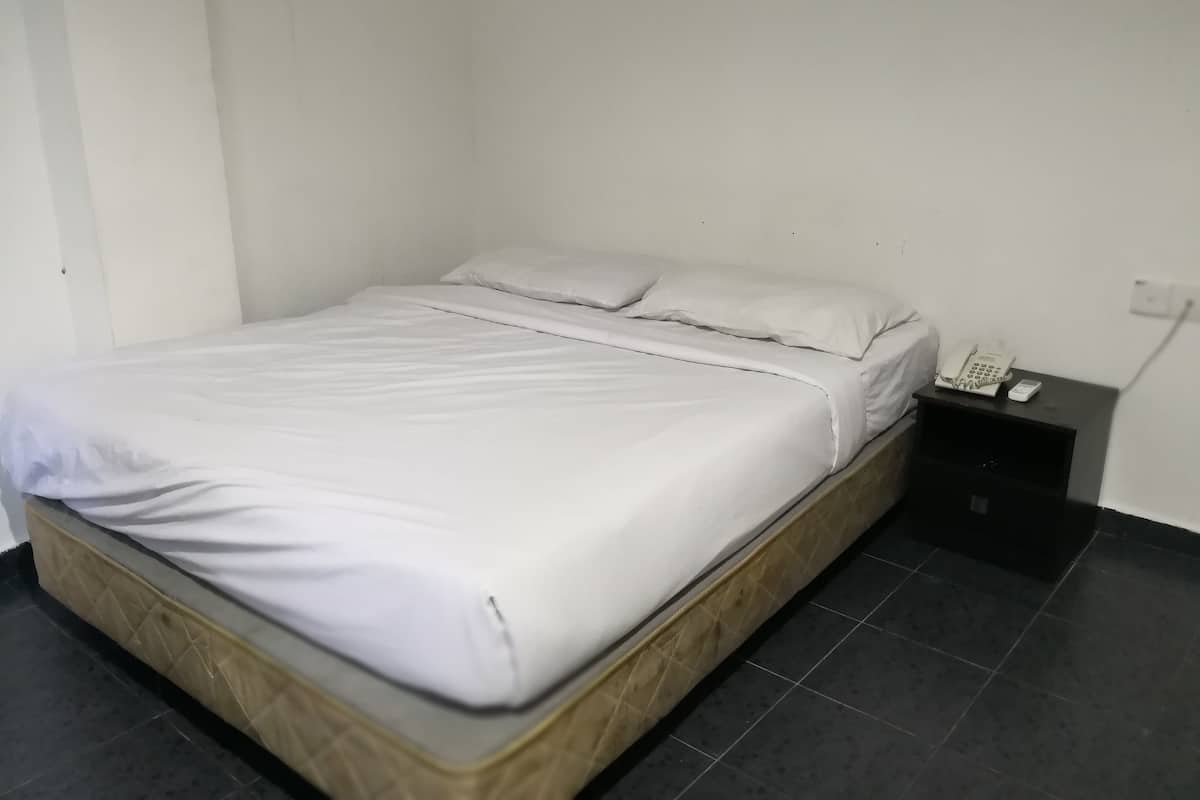 A single bed with a wooden frame and white bedding in a room with a tiled floor and a small bedside table with a telephone.