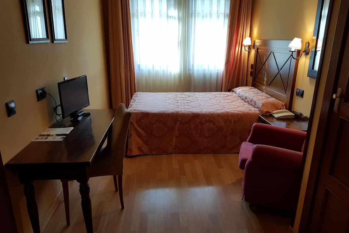 A hotel room with a bed, a desk with a computer, a chair, and a lamp.