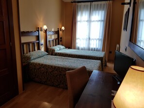 Una habitación de hotel con dos camas, un escritorio con lámpara, televisión y ventana con cortinas.