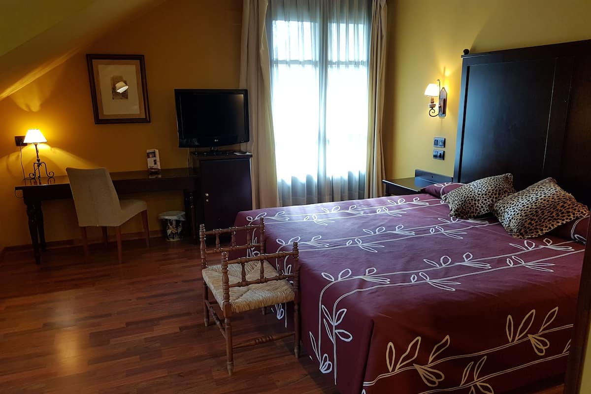 A hotel room with a large bed, a desk with a chair, a television, and a window with curtains.