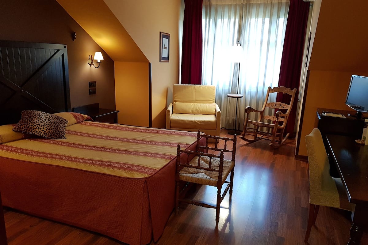A bedroom with a large bed, a wooden rocking chair, a small table, and a desk with a computer.