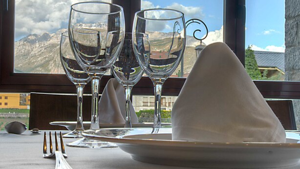 A table set for two with wine glasses and a plate, overlooking a mountainous landscape through large windows. - Hotel Cotiella (Campo)