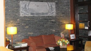 A lobby with a stone wall, a sofa, two armchairs, a coffee table, and lamps. - Hotel Cotiella (Campo)
