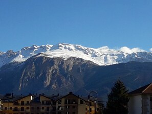 Una montaña con picos nevados al fondo, una calle con edificios en primer plano.