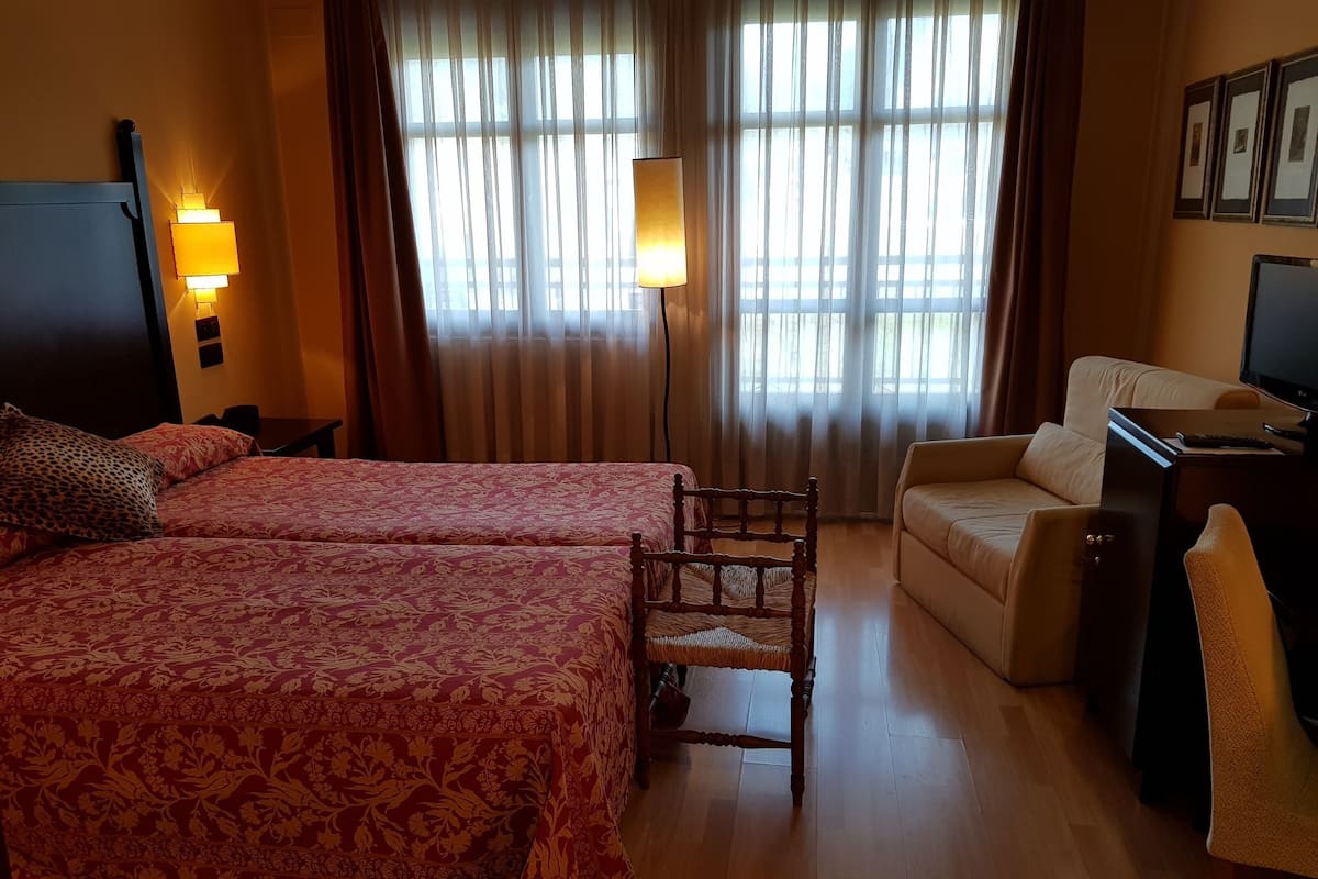 A hotel room with two beds, a desk, a chair, and a TV.