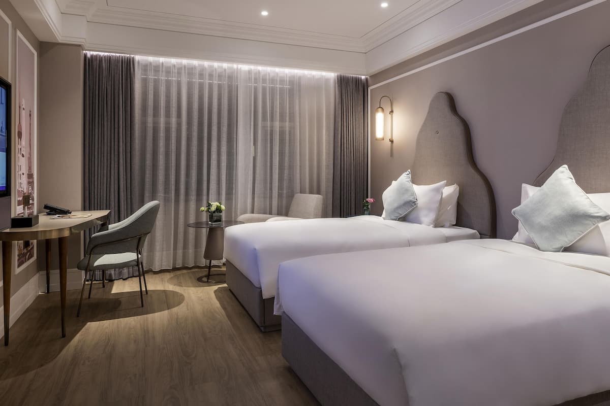 A hotel room with two beds, a desk, a chair, and a television.