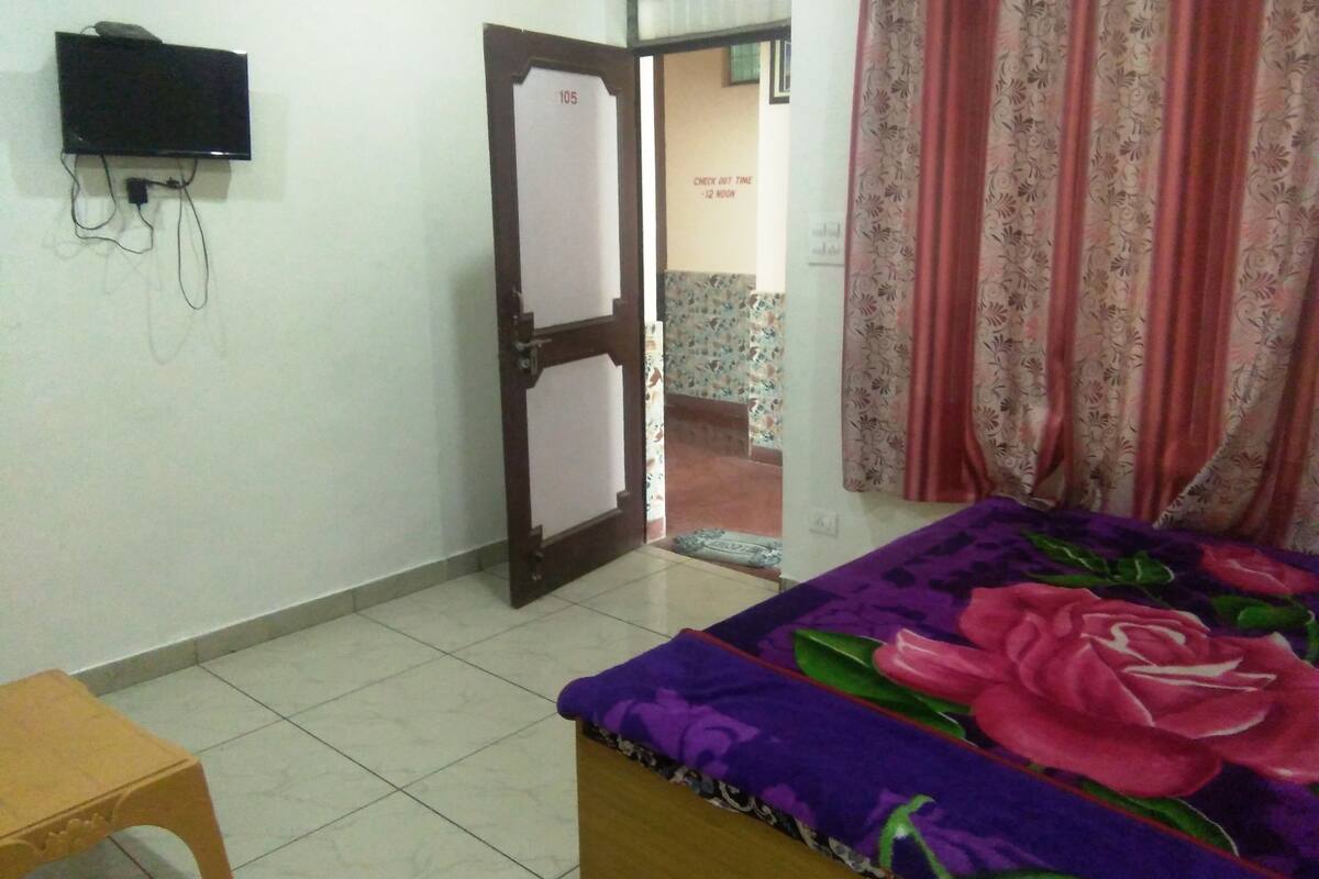 A bedroom with a bed, a wooden chair, a television on the wall, and a door leading to another room.