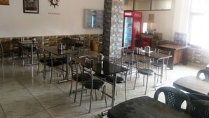 Um restaurante com várias mesas e cadeiras, uma geladeira Coca-Cola e uma placa na parede indicando 'Sem Álcool'.