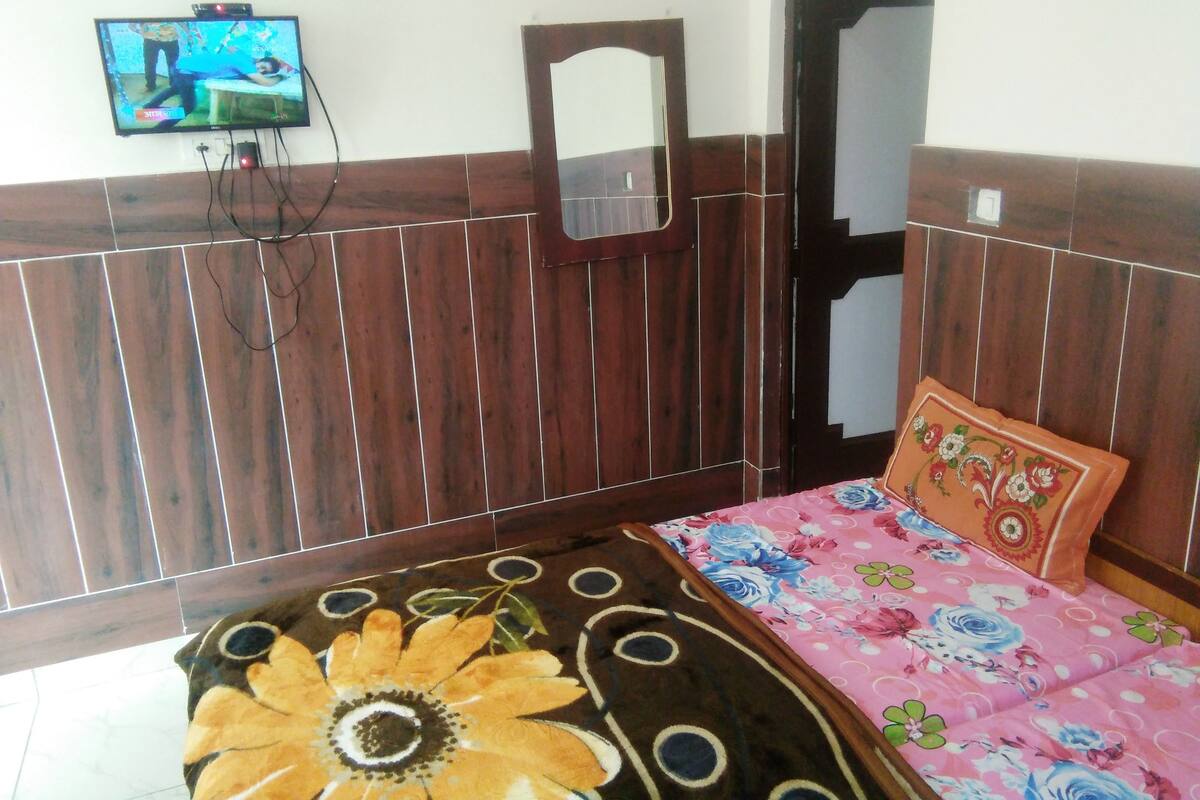 A bedroom with a wooden headboard, a bed with a floral bedspread, a television on the wall, and a mirror above the bed.