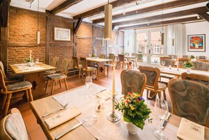 Un restaurante con mesas y sillas de madera, centros de mesa con velas y una pared de ladrillo.