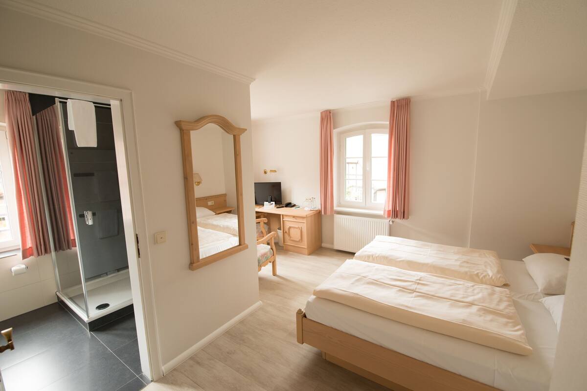 Un dormitorio con cama, escritorio, silla, espejo y ventana con cortinas.