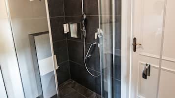 A modern shower with a glass door, a towel hanging on the door, and a white door next to it.