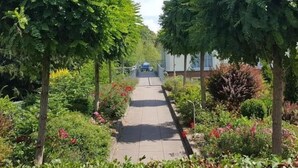 Un sentier bordé d’arbres et de plantes à fleurs, qui mène à un bâtiment.