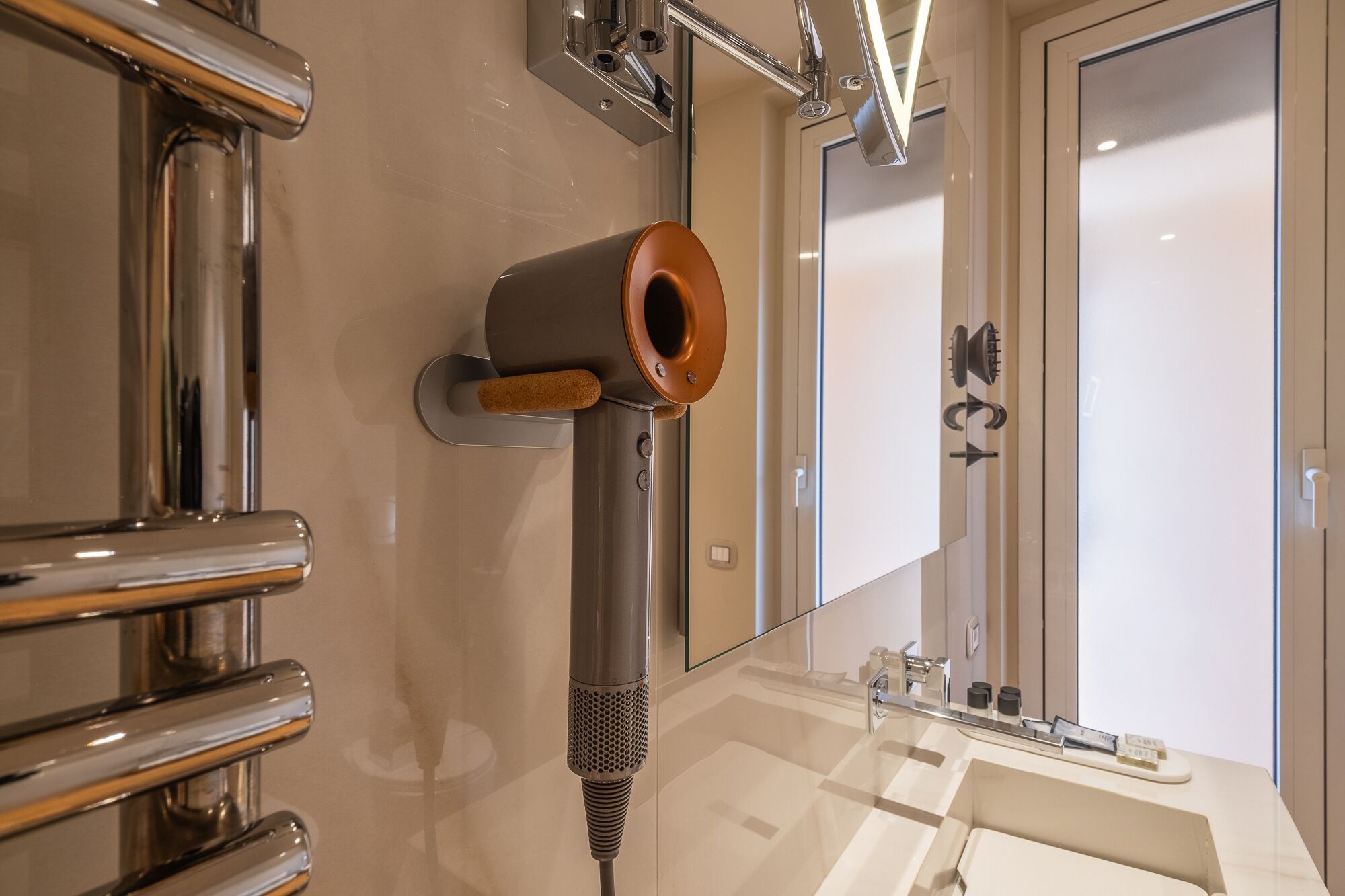 Une salle de bain moderne avec un sèche-cheveux fixé au mur, un grand miroir et un lavabo avec un meuble-vasque.
