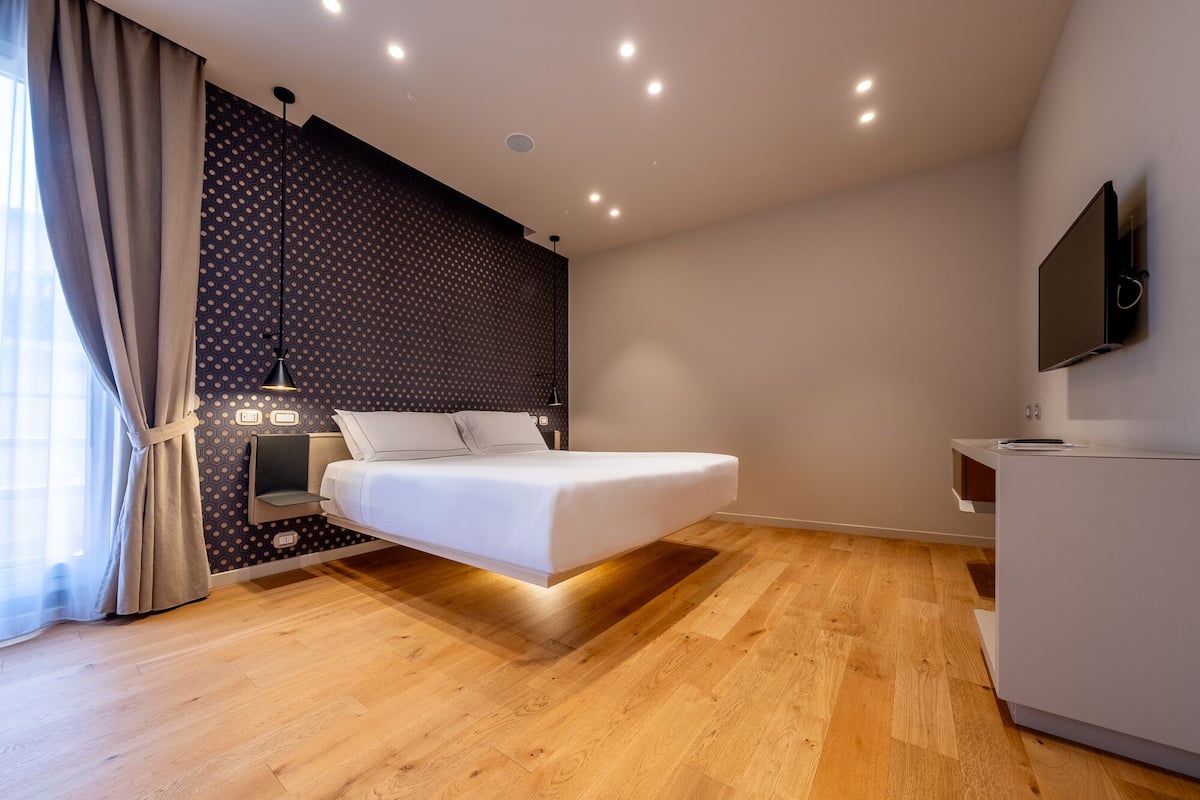 Una habitación de hotel moderna con una cama, un escritorio, un televisor y un papel tapiz estampado.