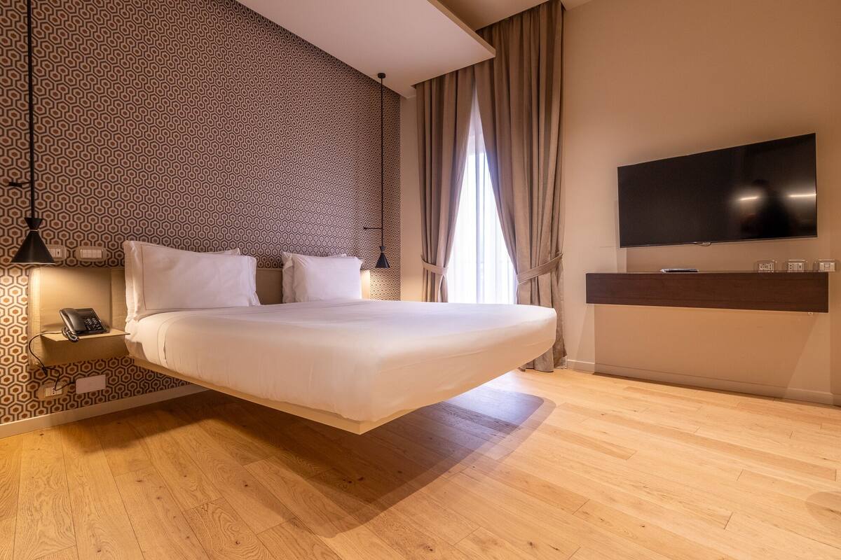 Un dormitorio moderno con una cama colgante, un teléfono en la mesita de noche, un televisor montado en la pared y un papel tapiz estampado.