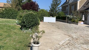 Een erf met een geplaveid pad, een witte constructie en verschillende planten.