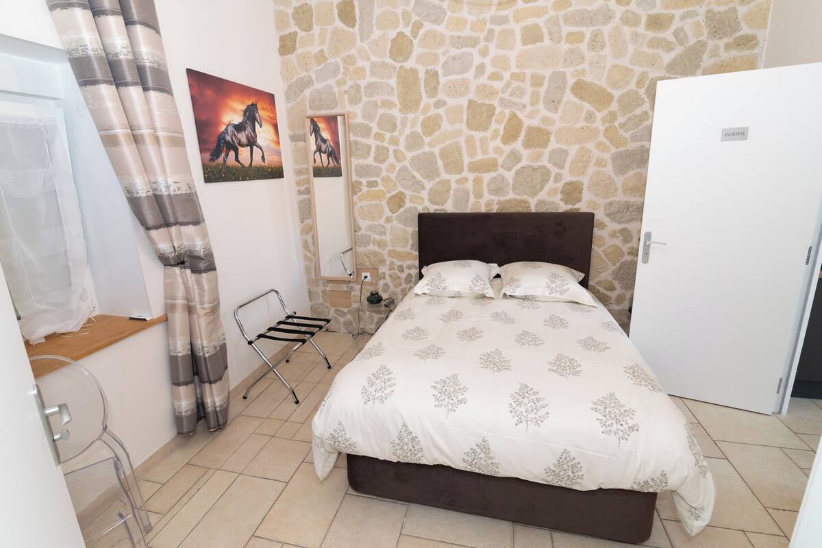 Un dormitorio con pared de piedra, cama con colcha estampada, puerta blanca y ventana con cortinas.