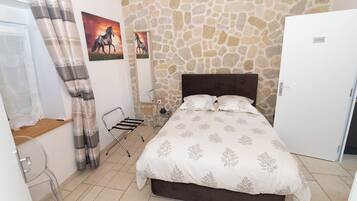 A bedroom with a stone wall, a bed with a floral bedspread, a white door, and a window with curtains.